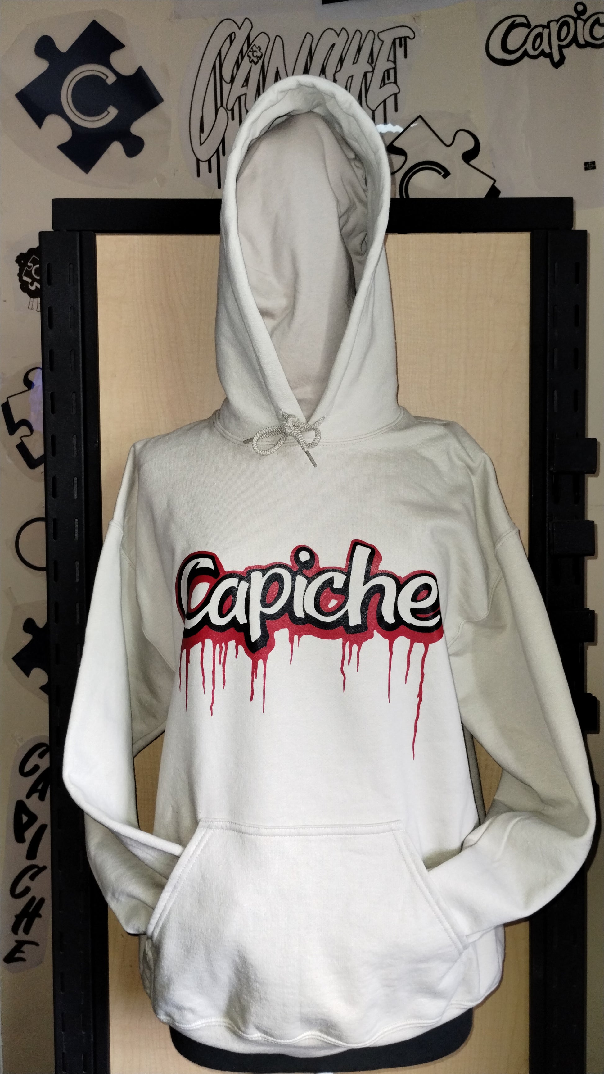 Front view of tan hoodie on manikin. Two tone Capiche logo in black and red ink.