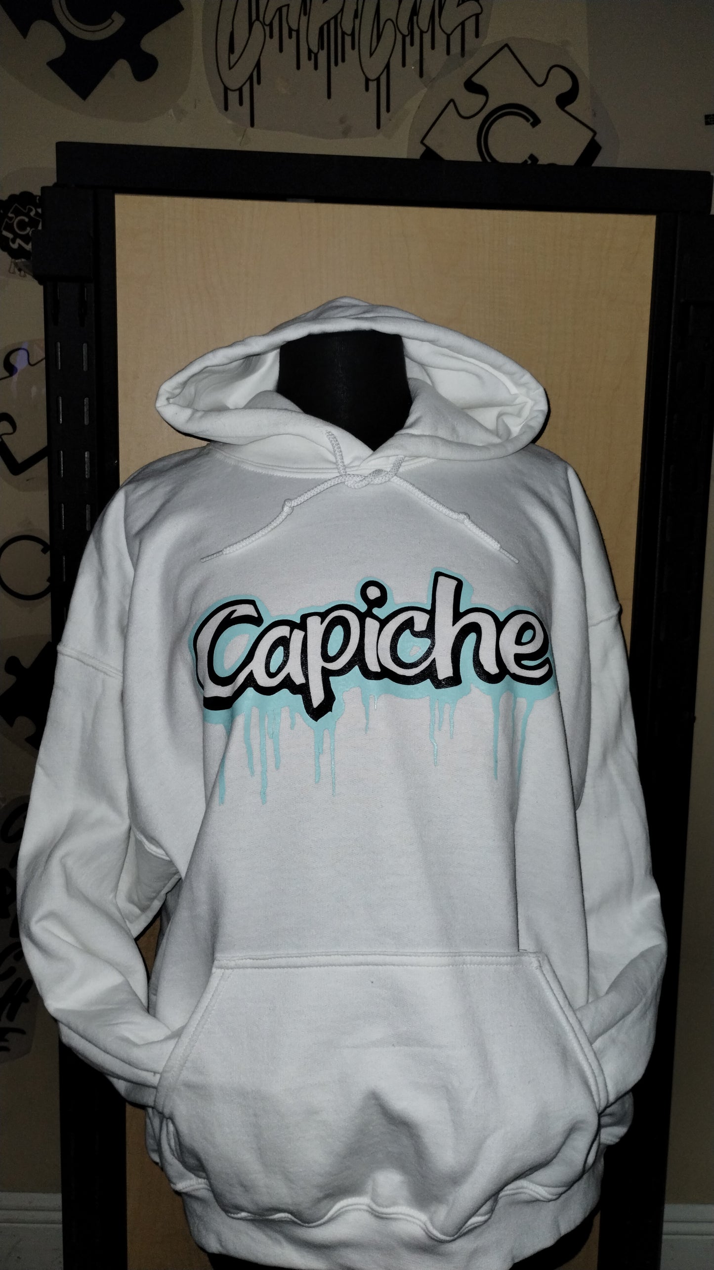 Front view of white hoodie on a manikin. Capiche logo in black and teal ink