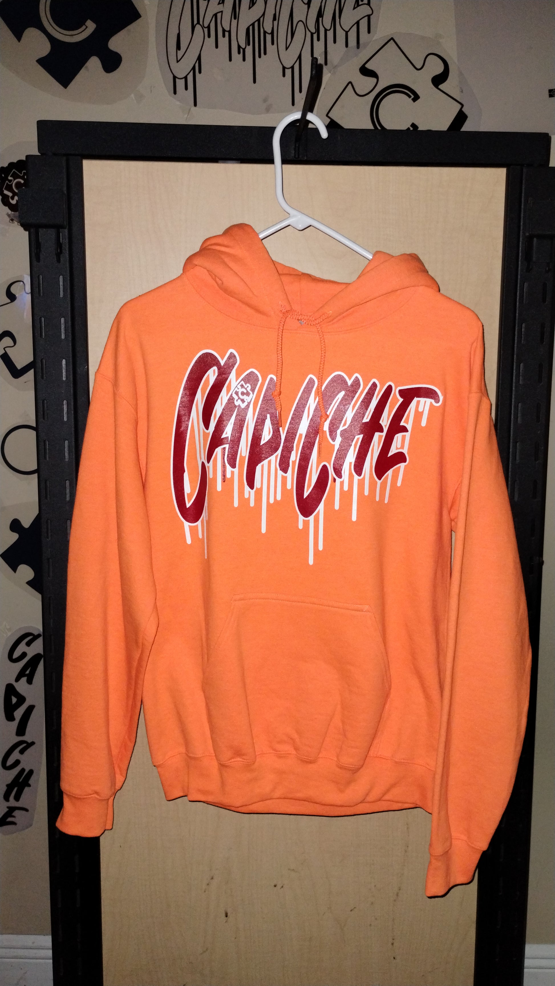 Front View of Orange hoodie on a hanger. Capiche logo in red and white ink.