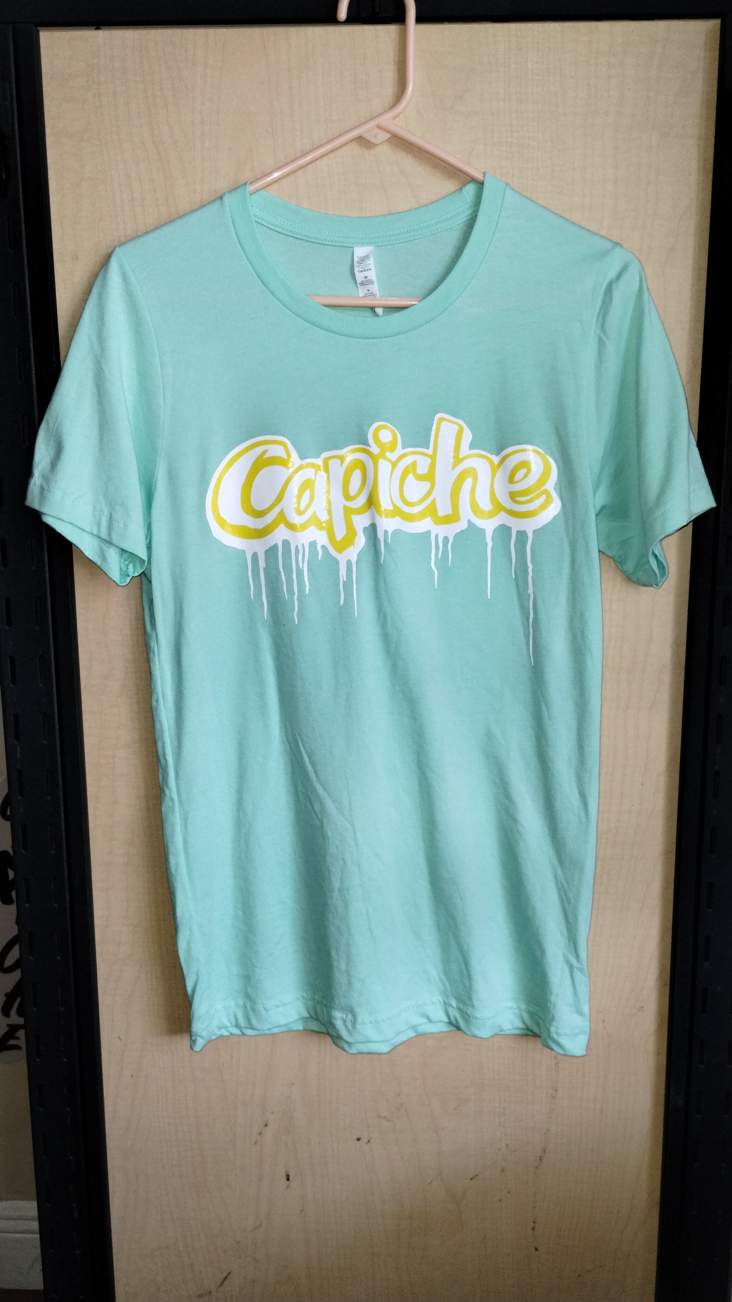 Mint Color Tshirt on a hanger. Capiche logo printed on the front in banana yellow and white ink.