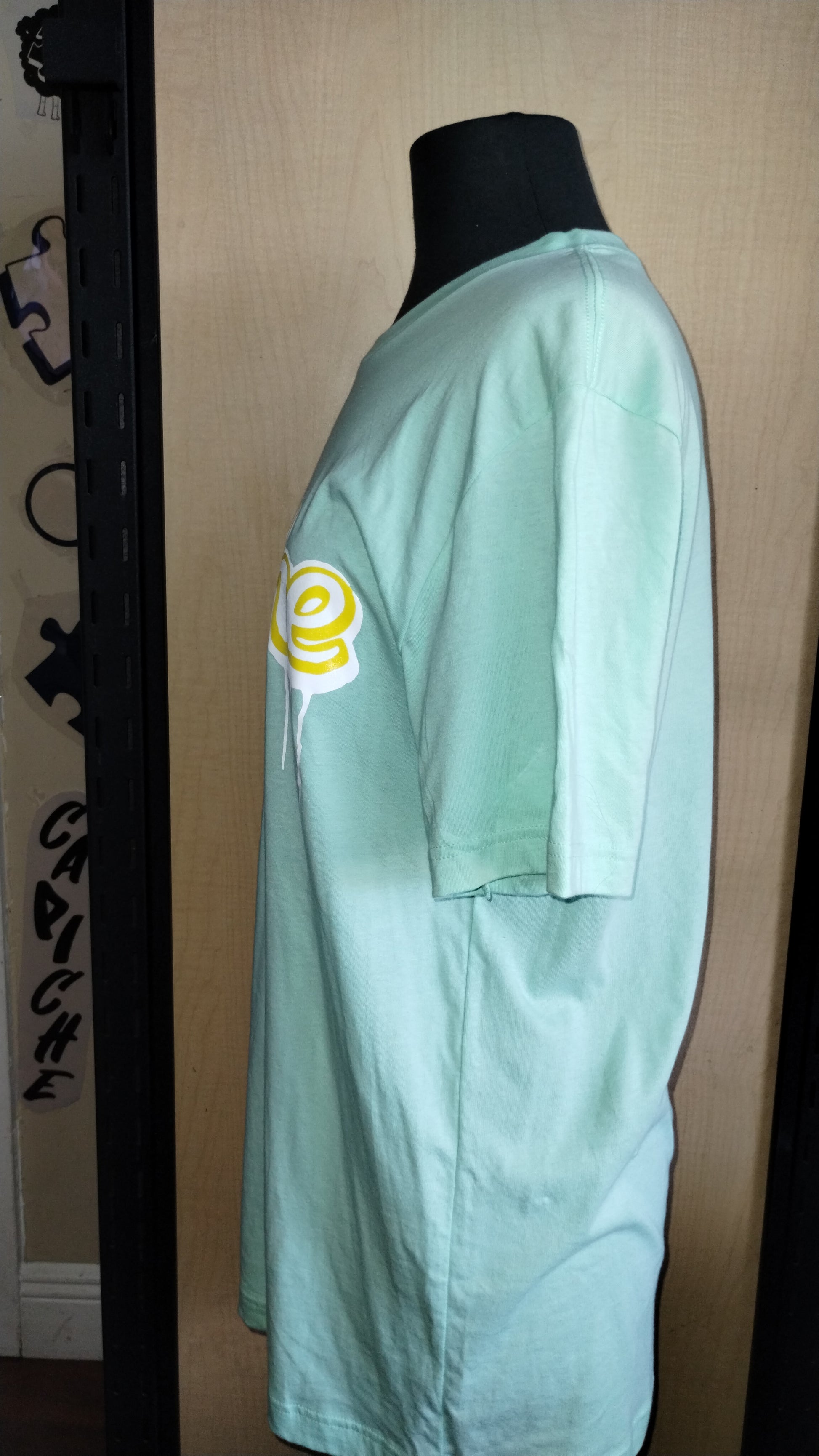 Side view of shirt on a manikin. Mint Color shirt with capiche printed in banana yellow and white ink.