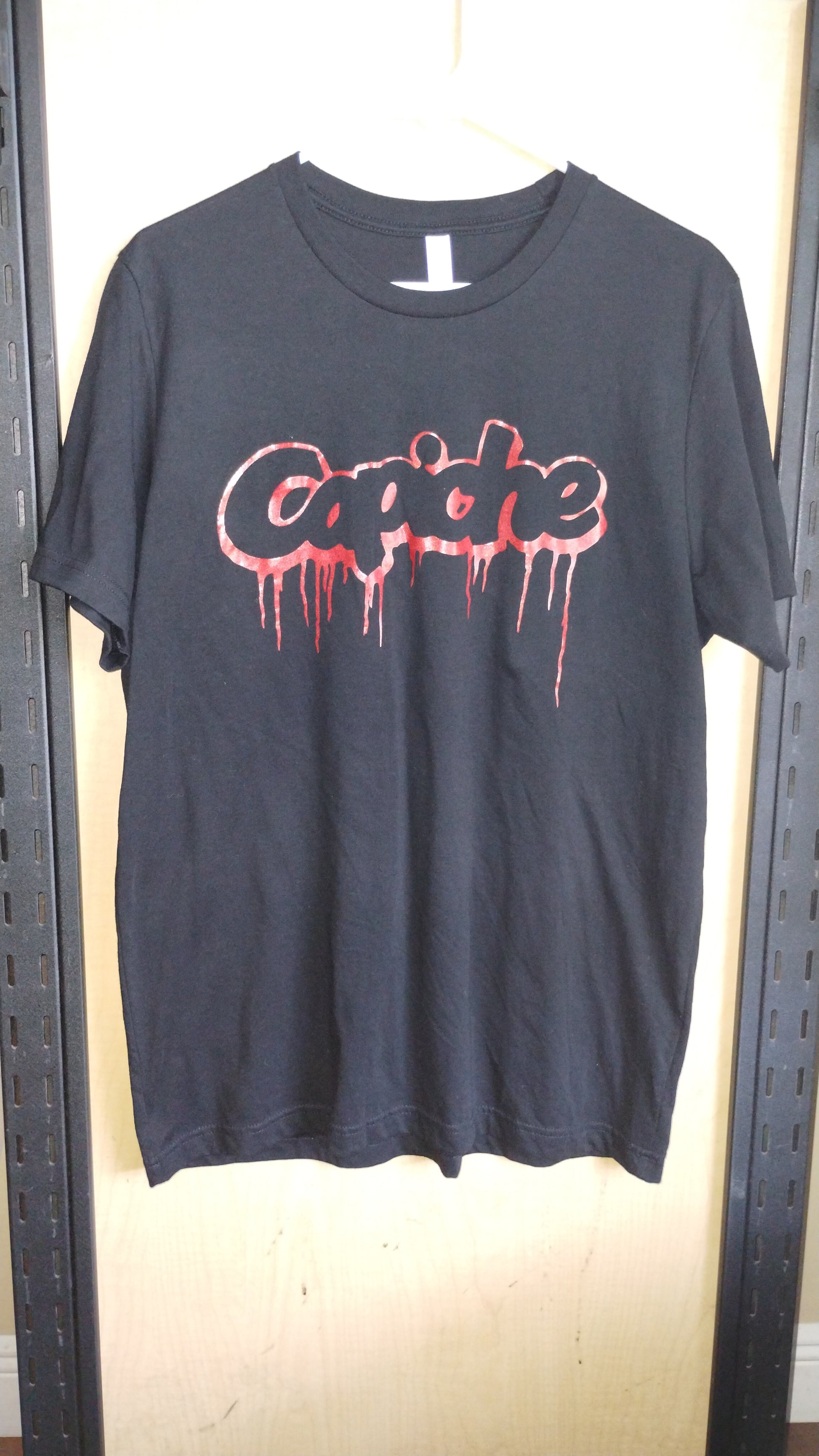 Black Tshirt on a hanger. Capiche logo printed on front in red ink.