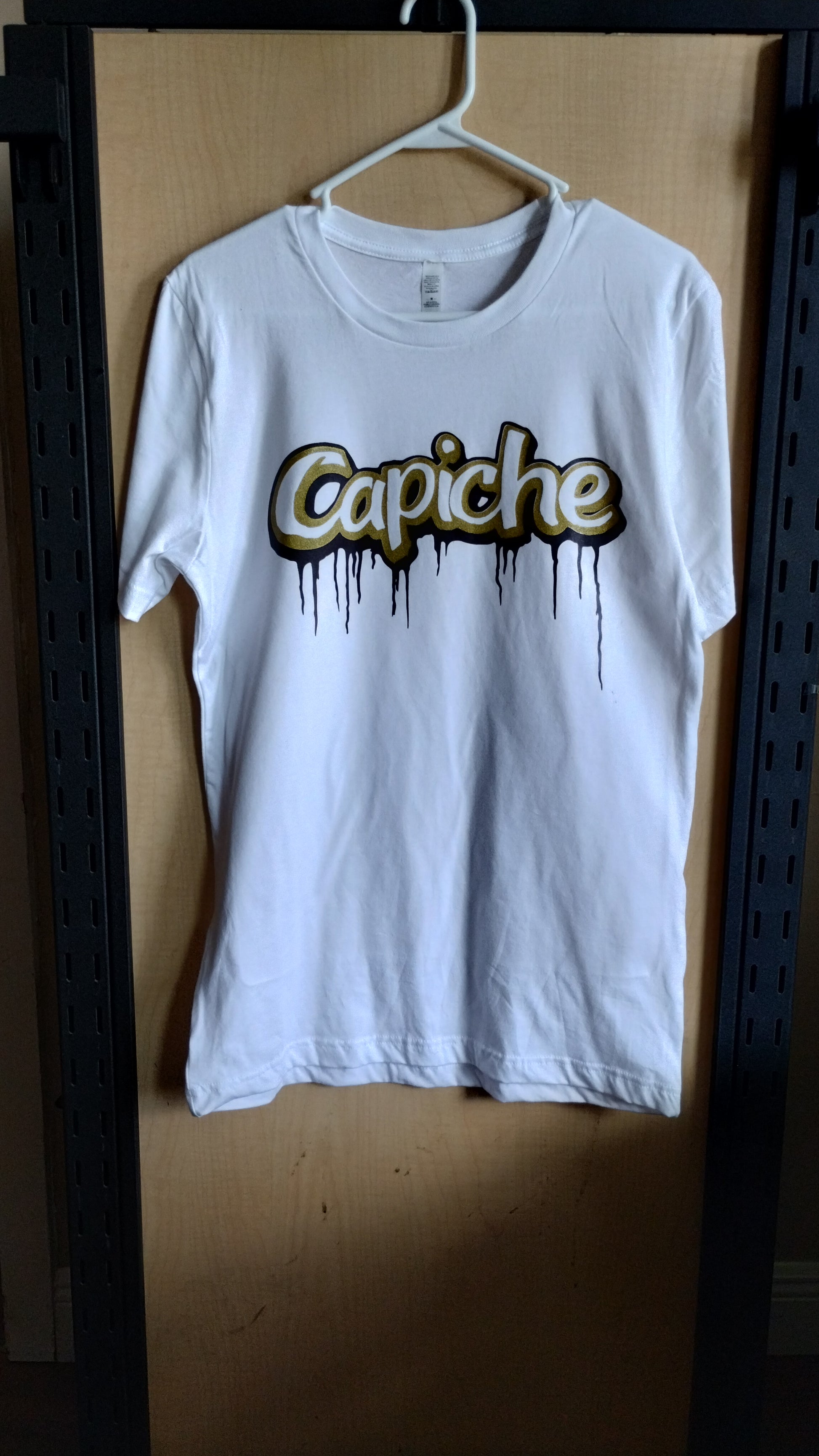 Front view of a White Tshirt on a hanger. Capiche logo printed on the front with gold and purple ink.