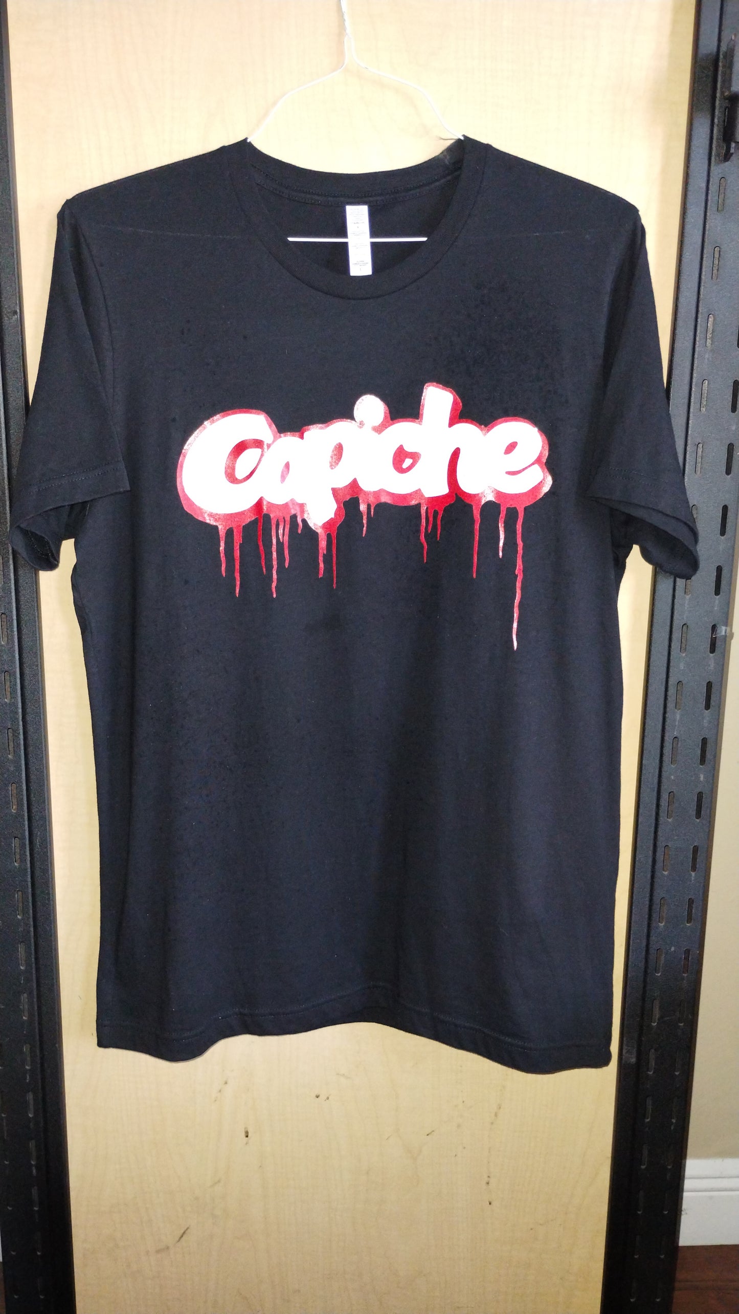 Front view of black shirt on a hanger with the Capiche logo printed in red and white inks.